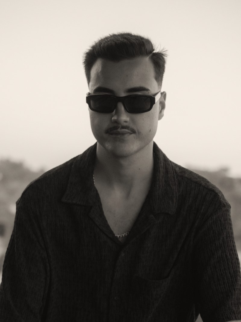 Retrato de Crazypapi, de óculos escuros e camisa preta, ao pôr do sol